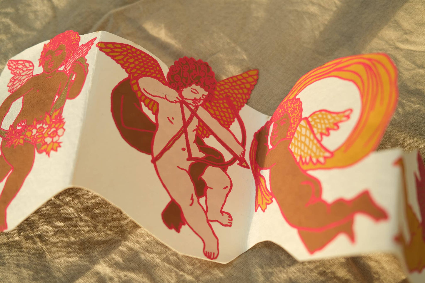 Cupid Concertina Card. This greeting card unfolds to reveal a row of cheeky cherubs. There is a panel for your message on the reverse, and a beautiful matching envelope with a luxe gold printed pattern.