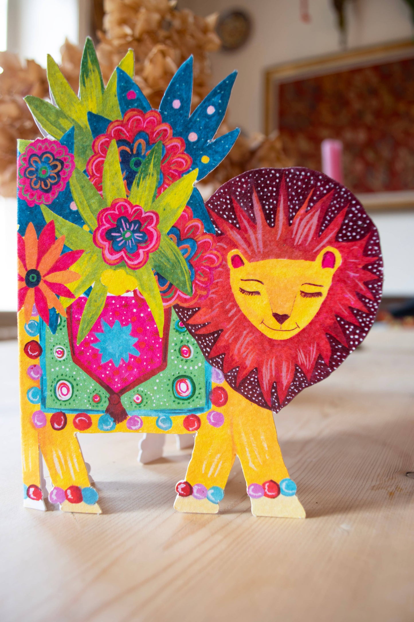 'Lion Parade' Die-Cut Greetings Card. A beautiful smiling lion, carrying the biggest bunch of colourful flowers on his back. The lion is adorned with a colourful blanket.