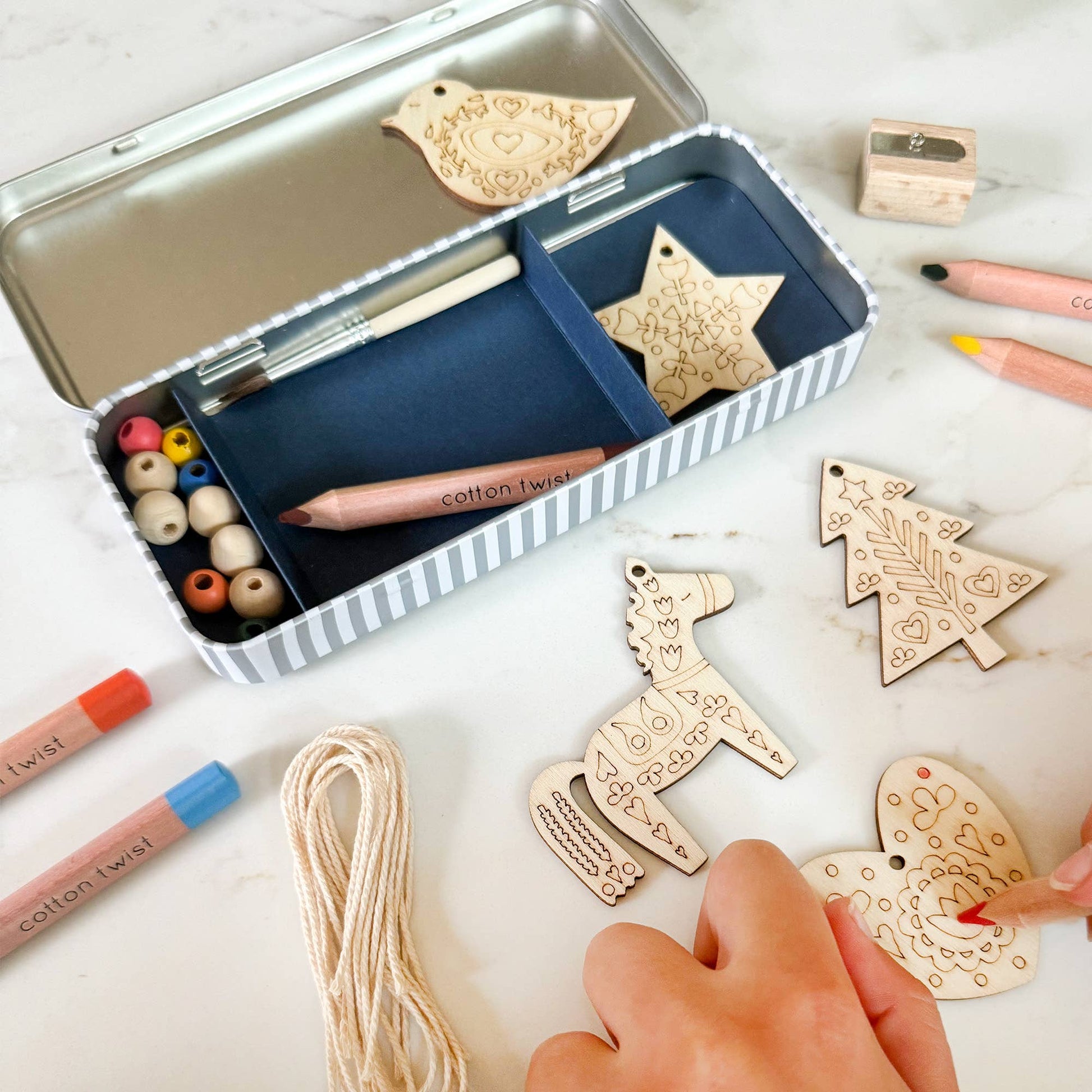 Folk Art Decoration kit. This kit features five wooden decorations to make, perfect for adding a touch of handcrafted beauty to a Christmas tree or any festive display. Along with the wooden decorations, the kit includes a selection of watercolour pencils and wooden beads, allowing for each decoration to be personalised with a touch of folk art charm.