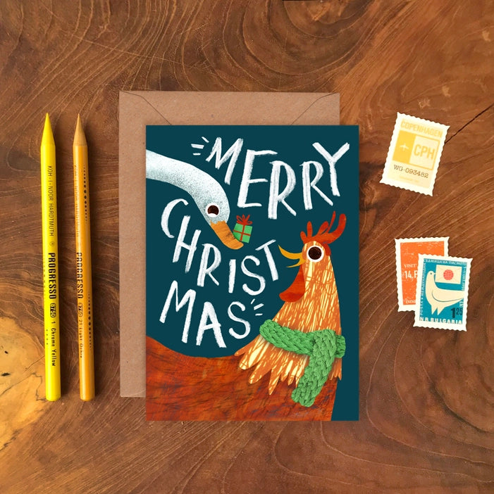 Illustrated Christmas greeting cards by Emily Nash Illustration. With the words Merry Christmas. featuring a goose, presenting a gift to his friend a hen in a green cosy scarf. 