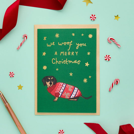 This cute Christmas card of an adorable sausage dog wearing a Christmas jumper? original card features a hand drawn illustration of a miniature dachshund sporting a knitted festive sweater, painted in traditional seasonal colours.
The message on the front of this read We woof you a merry Christmas.