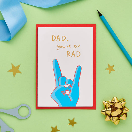 This dad card offers a heartfelt greeting that's just a little bit different from your usual greetings cards. Hand drawn design features a hand in a 'rock on' pose. Painted in bright colours with a striking, hand lettered font and finished with gold foil, the message on the front of this funny dad card reads "Dad, you're so rad".