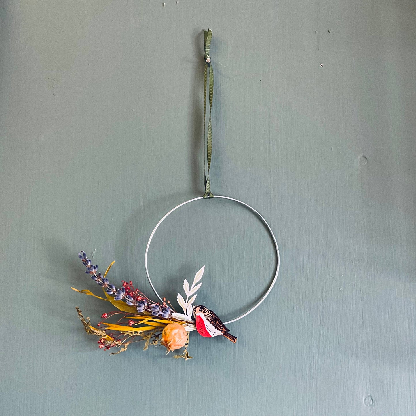 The robin come to life when we laser cut and engrave them from wood, hand painting their features. The wreath is made from steel wire that is hand shaped, we then secure a posy of dried flora and paper leaves. Lastly we affix your Robin and tie a piece of ribbon so it can be hung up.