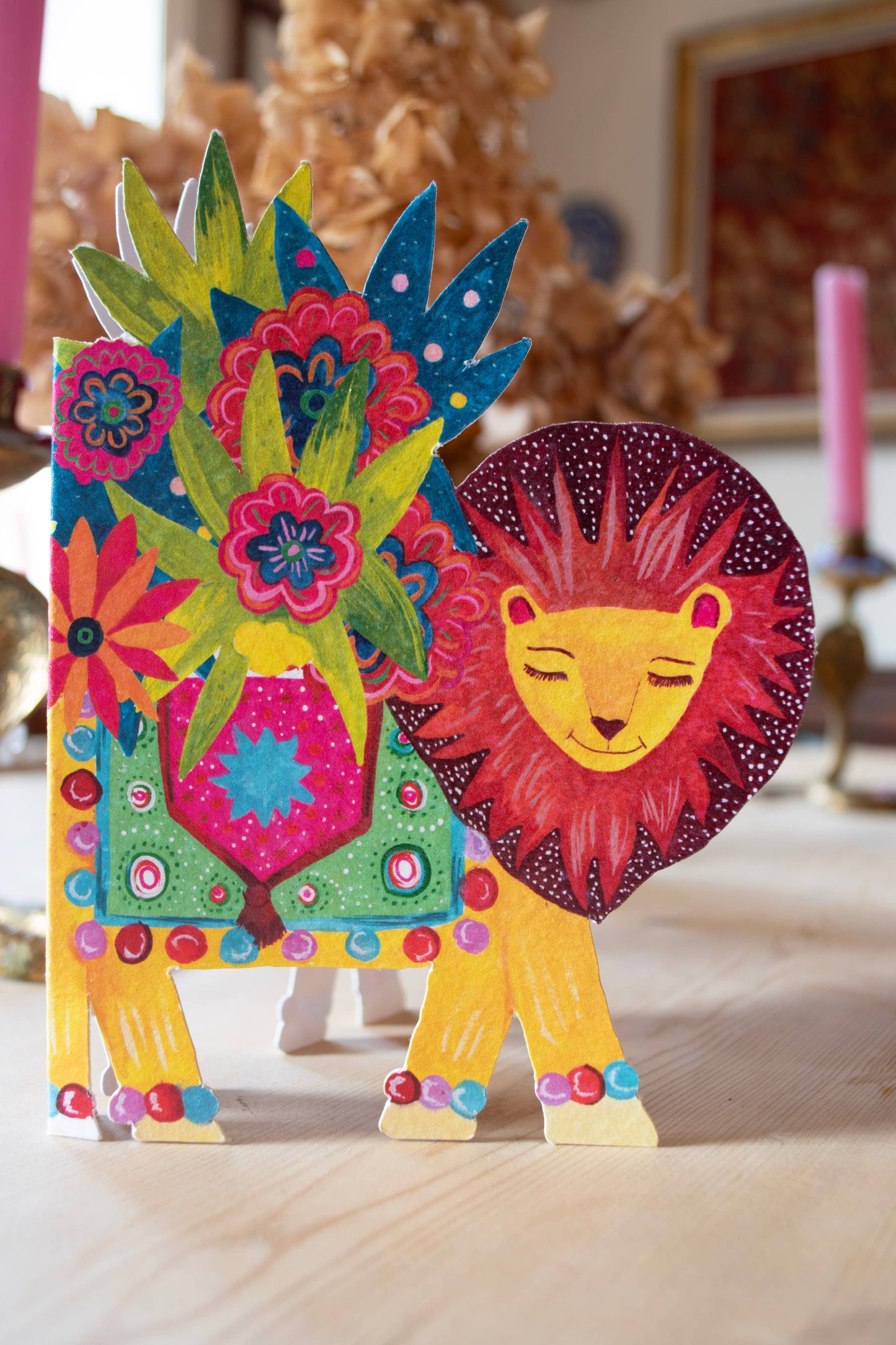 'Lion Parade' Die-Cut Greetings Card. A beautiful smiling lion, carrying the biggest bunch of colourful flowers on his back. The lion is adorned with a colourful blanket.