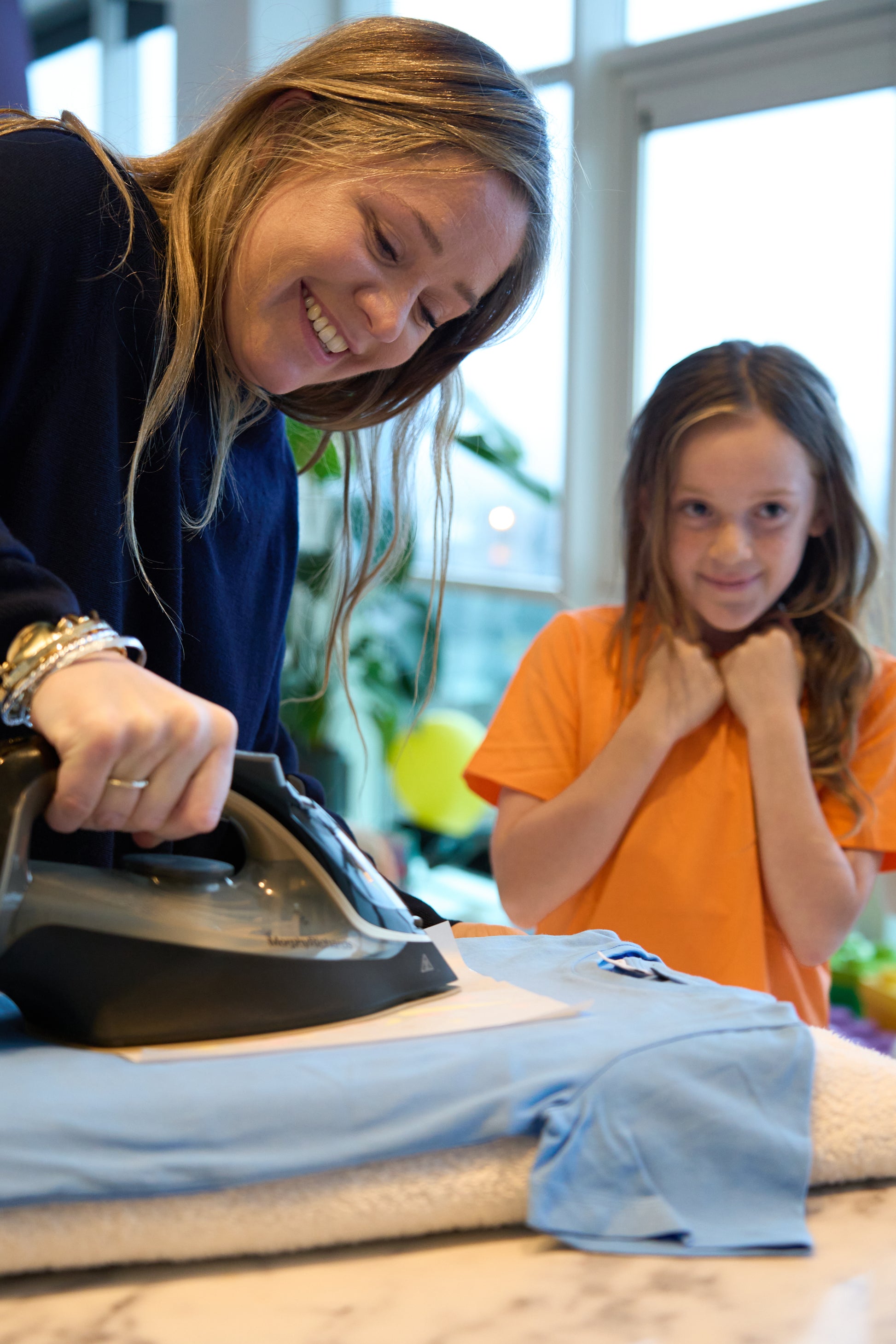 An adult irons on the Unicorn Potkit onto a blue t-shirt whilst the child looks on in anticipation.