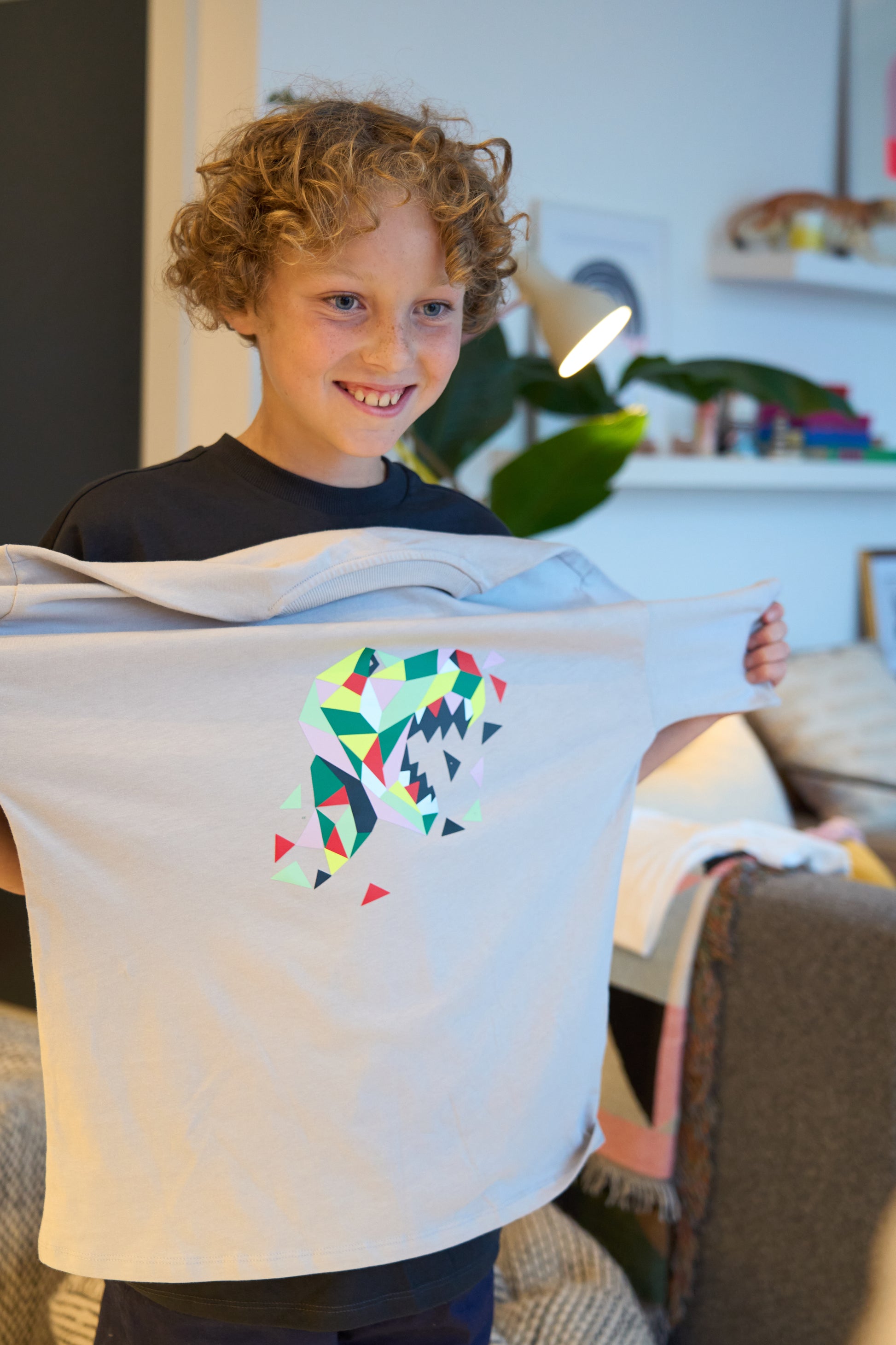 The child proudly holds up the completed Dinosaur on a grey tshirt.