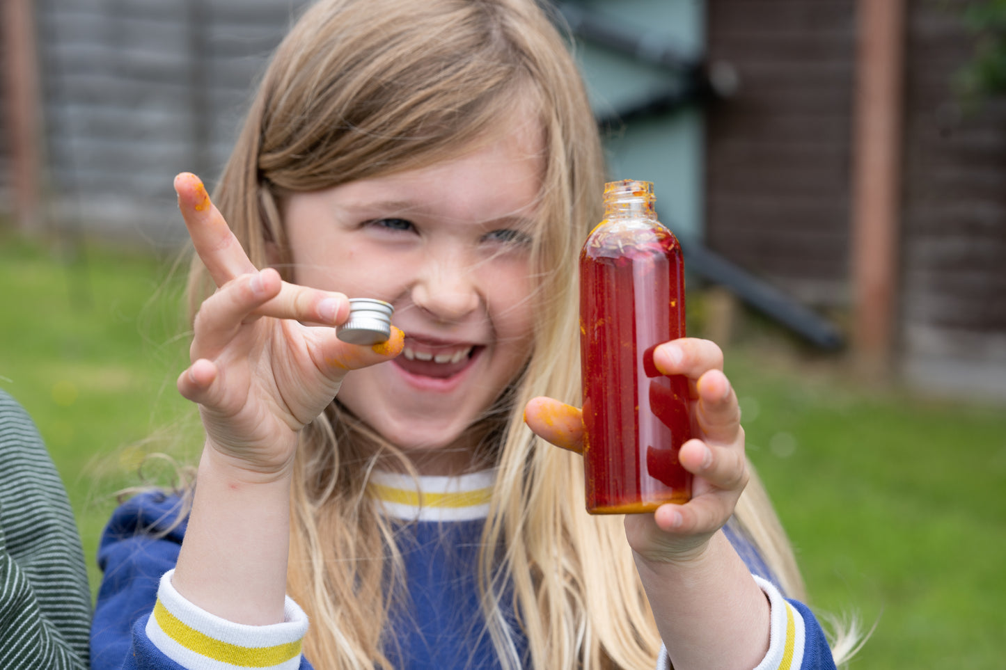 A smiling child shows off her bottle of red potion, she has made using the Potion Kit.