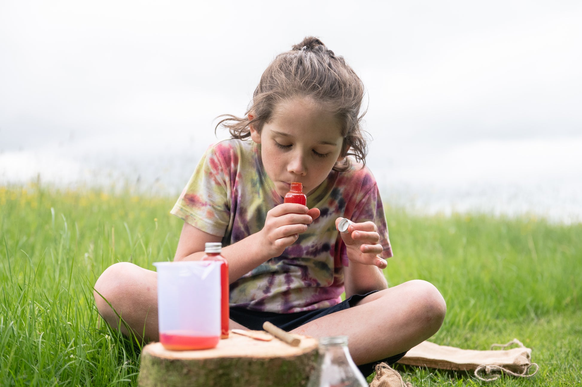 A  child smells the bottle of red potion, she has made using the Potion Kit.