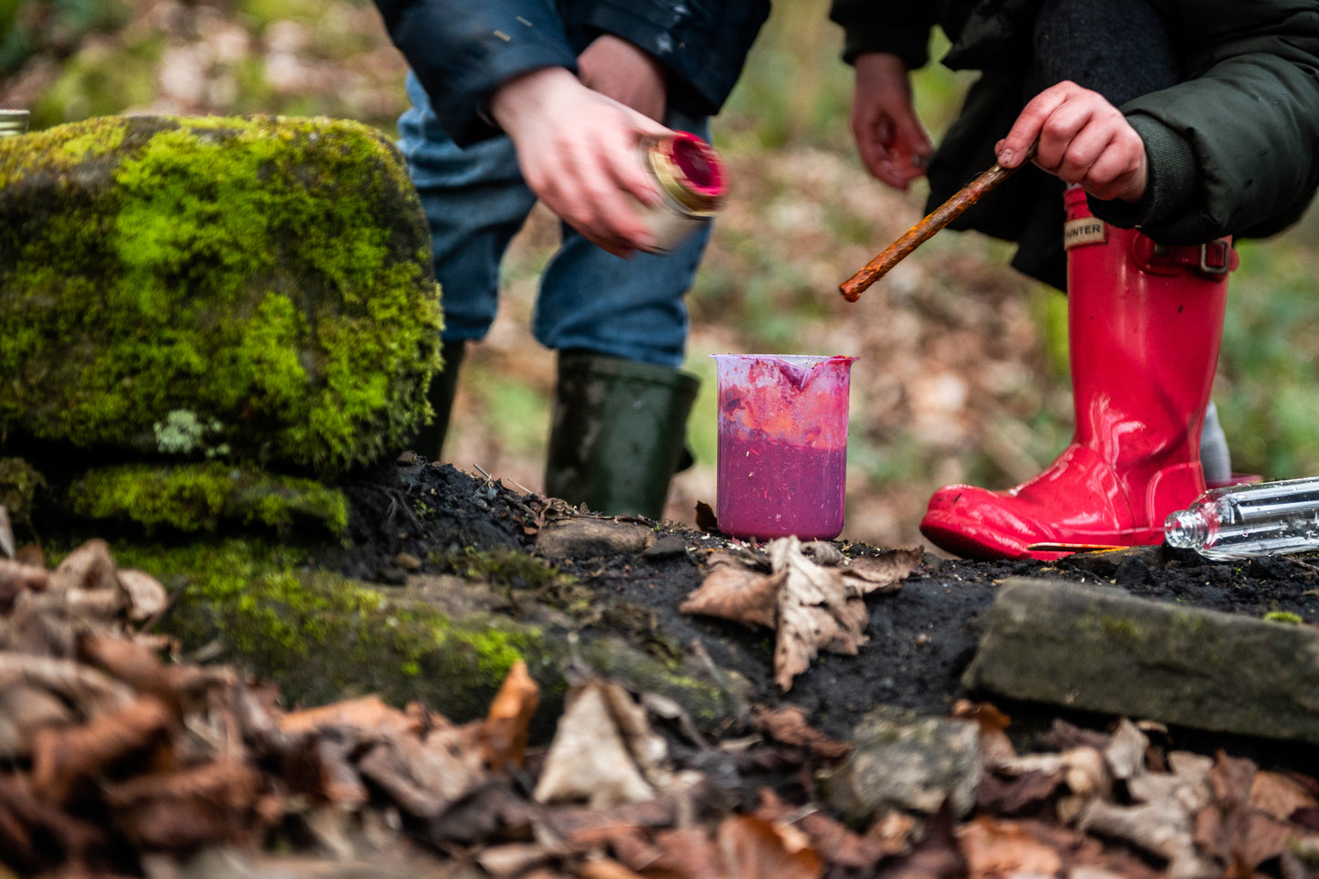 Children making potions in the woods, dressed in their welly boots.