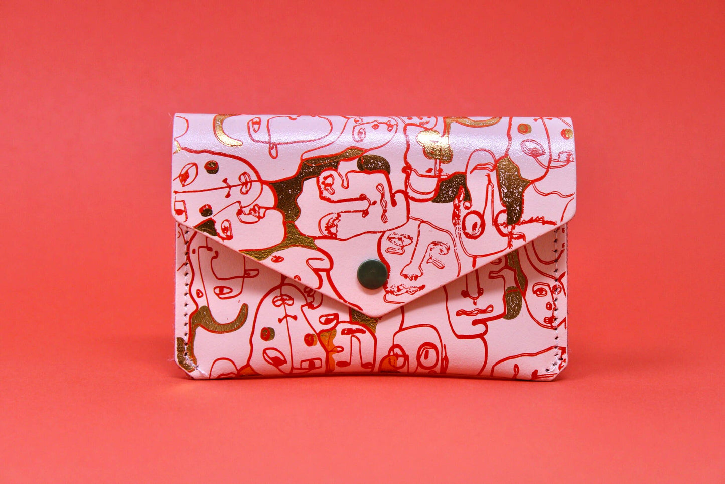 A small leather purse embossed with a wrap around figurative design. The simple line illustration features a collection of different characters. Purse is pale pink with gold embossed detail and patches of red