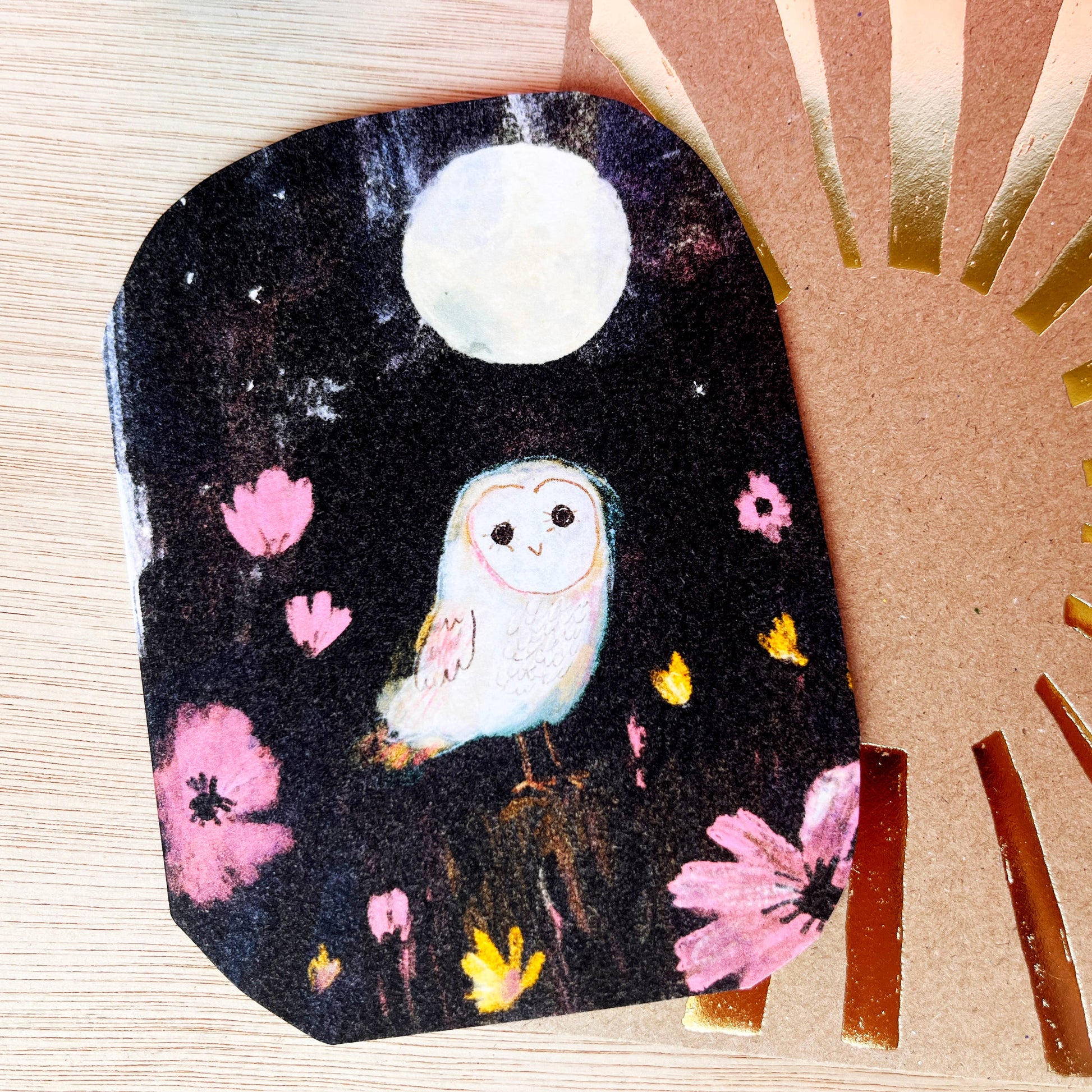 Illustrated card of a snowy owl against a dark sky with a full moon. Looking happy amongst the flowers and moonlight. 