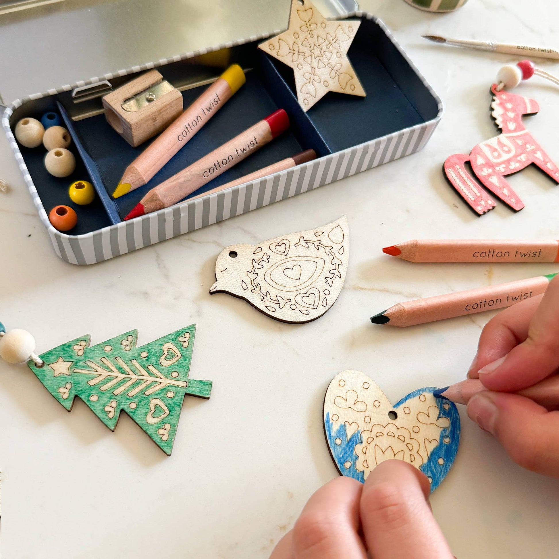 Folk Art Decoration kit. This kit features five wooden decorations to make, perfect for adding a touch of handcrafted beauty to a Christmas tree or any festive display. Along with the wooden decorations, the kit includes a selection of watercolour pencils and wooden beads, allowing for each decoration to be personalised with a touch of folk art charm.