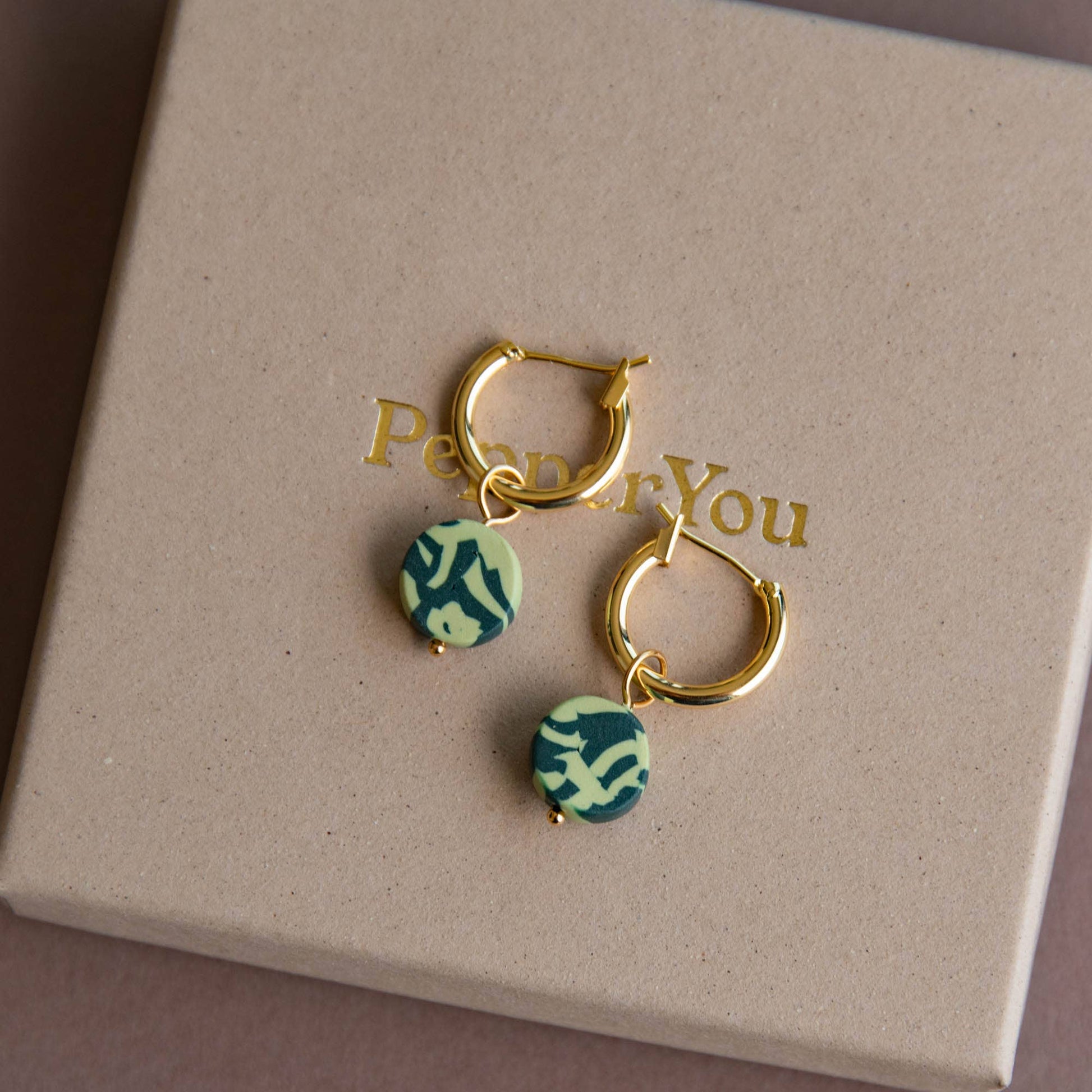 Bits Circle Charm Hoop Earrings. Gold  plated nickel free earring hoops. With a circle of handmade pigmented clay which is mixed together to create this fun jumbled pattern. Shown in Forest and Apple Green with a Pepper you box.