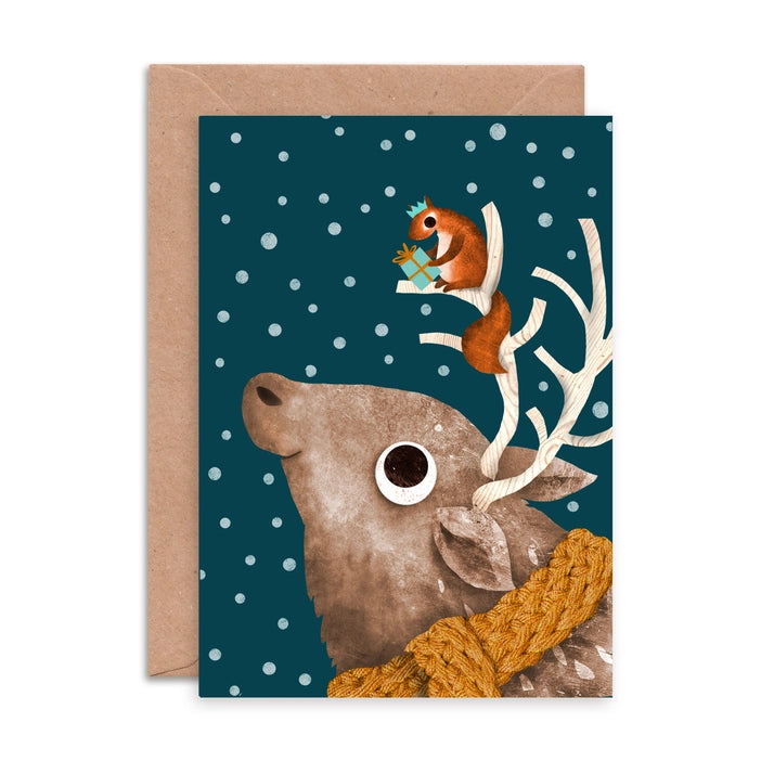 Illustrated Christmas greeting cards by Emily Nash Illustration. With the words Merry Christmas. featuring a squirrel in a Christmas hat, presenting a gift to his friend a deer in a mustard cosy scarf. All the while the dark sky is filled with snow.