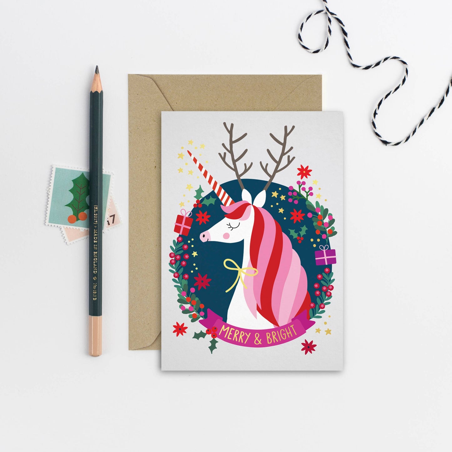 Merry and Bright Unicorn Holiday Card. This illustrated Christmas card adds an extra bit of magic to the holiday season with a gorgeous unicorn as the centrepiece. Smiling sweetly from within the holiday card’s festive swirl of foliage, gifts and a banner with gold foil “Merry &amp; Bright” caption, the unicorn also boasts a set of reindeer antlers and a gold ribbon.