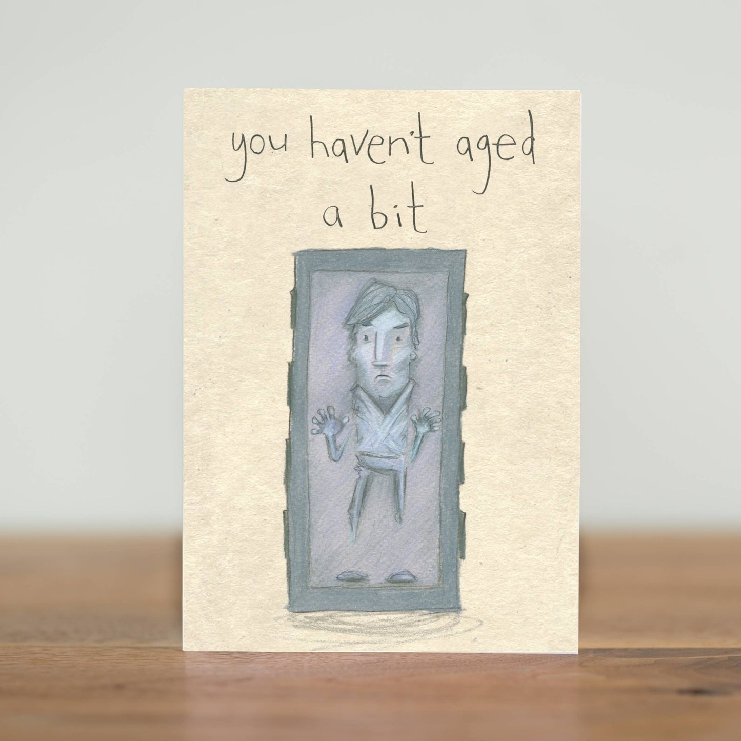 Illustrated card, featuring a youthful Han Solo. He may be down on his luck and frozen in carbonite, but he’s still as handsome as ever. With the words you haven't aged a bit